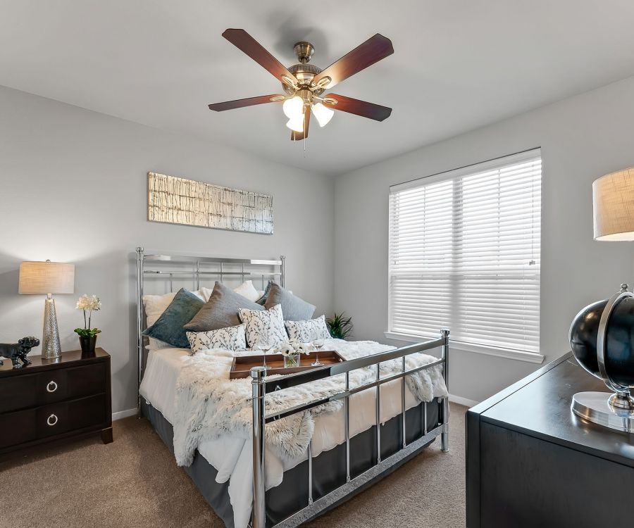 Gateway Cedars apartment bedroom with large windows, ceiling fan, and furnished with a bed and dresser