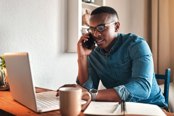 Focused man on phone while looking at laptop at home